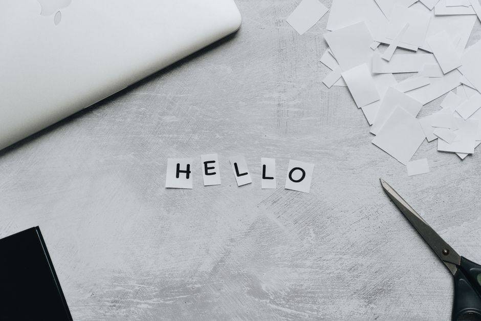 Flat lay of a creative workspace with scissors and cut out letters spelling 'hello' on a textured surface.